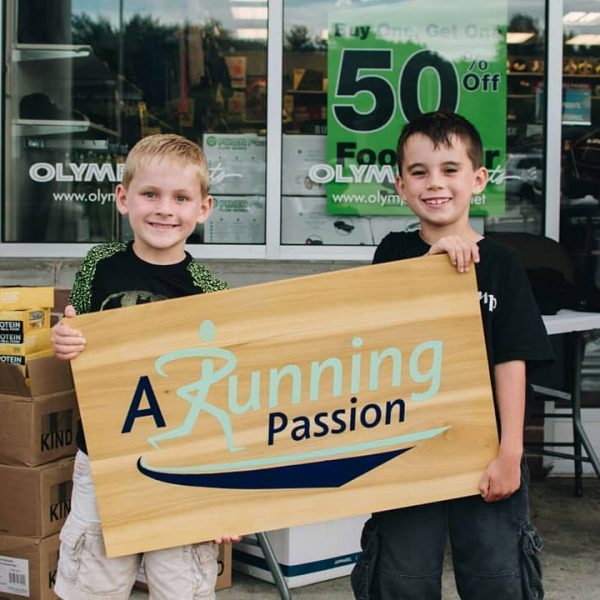 Two young boys holding an A Running Passion sign